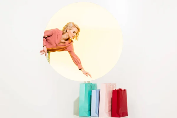 Bela menina elegante posando com sacos de compras coloridos no branco com círculo amarelo — Fotografia de Stock