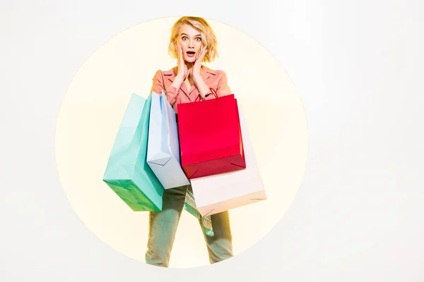 Sorprendida chica con estilo mirando a la cámara y sosteniendo bolsas de compras en blanco con círculo amarillo - foto de stock
