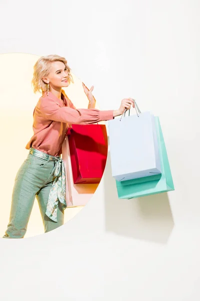 Hermosa chica elegante sonriendo y posando con bolsas de compras en blanco con círculo amarillo - foto de stock
