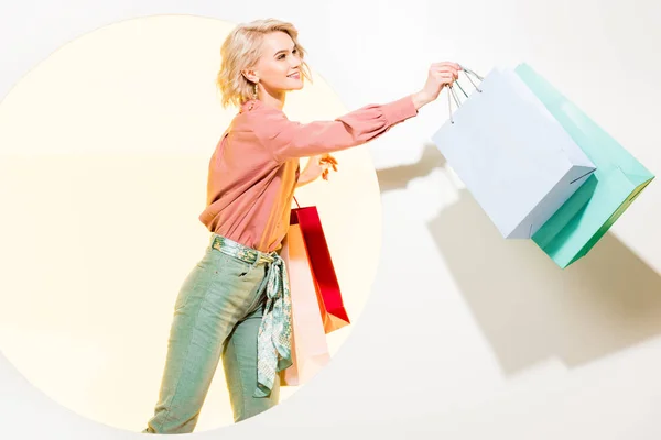 Beautiful stylish girl smiling and holding shopping bags on white with yellow circle — Stock Photo