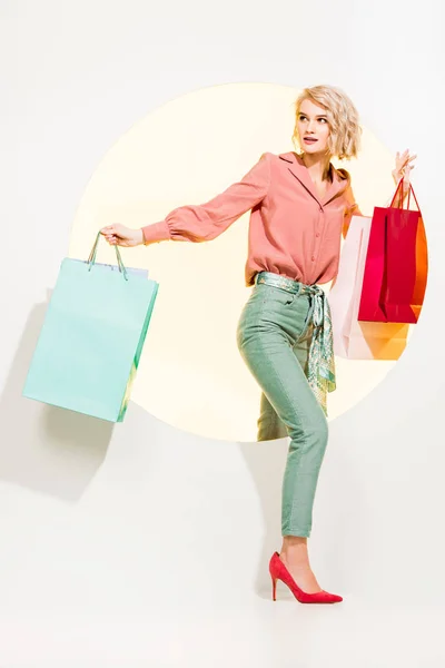 Hermosa chica con estilo con bolsas de compras caminando a través de círculo amarillo en blanco - foto de stock