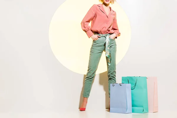 Recortado vista de elegante chica posando cerca de bolsas de compras en blanco con círculo amarillo - foto de stock