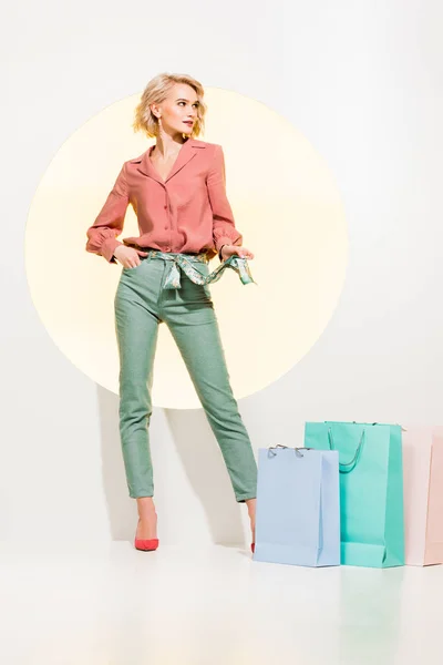 Beautiful fashionable girl posing near shopping bags on white with yellow circle — Stock Photo