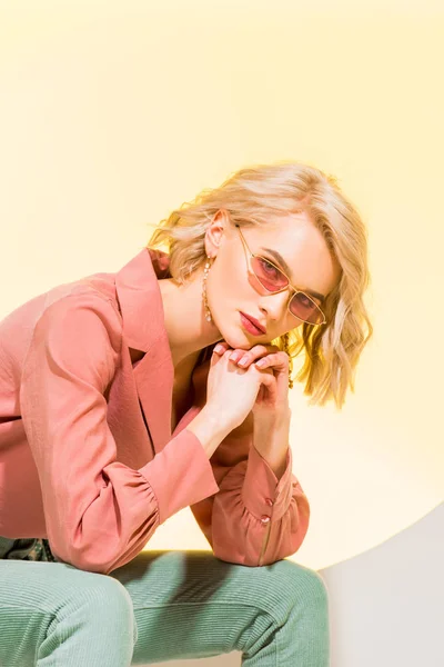Beautiful stylish blonde girl in coral jacket looking at camera and posing on yellow — Stock Photo
