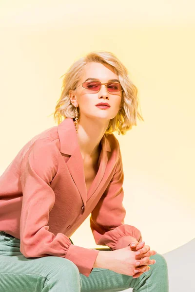 Hermosa chica con estilo en chaqueta de coral y gafas de sol posando en amarillo - foto de stock