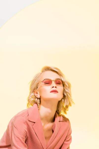 Beautiful stylish blonde girl in coral jacket posing on yellow with copy space — Stock Photo