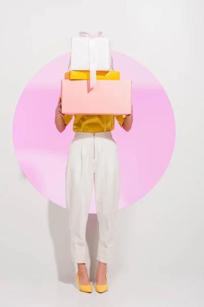 Elegante chica que cubre la cara con cajas de regalo en blanco con círculo rosa - foto de stock