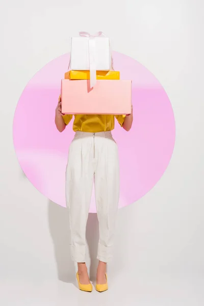 Stylish girl covering face with gift boxes on white with pink circle — Stock Photo