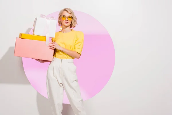 Hermosa chica elegante sosteniendo cajas de regalo en blanco con círculo rosa y espacio de copia - foto de stock