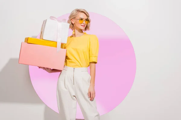 Beautiful stylish girl holding gift boxes on white with pink circle and copy space — Stock Photo