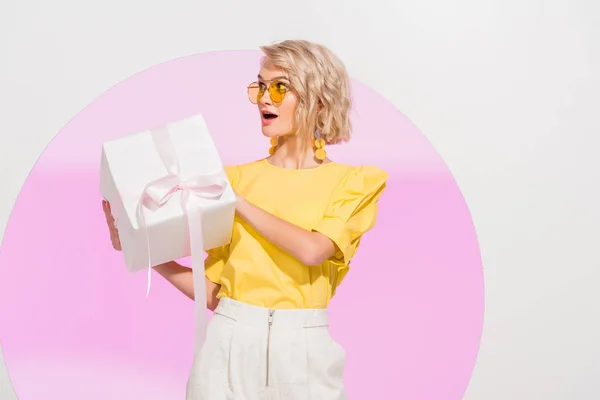 Excité fille élégante Holding cadeau boîte sur blanc avec cercle rose — Photo de stock