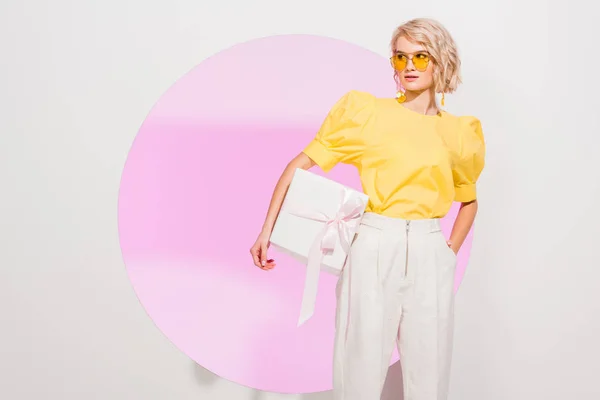 Bella ragazza alla moda in possesso di scatola regalo su bianco con cerchio rosa — Foto stock