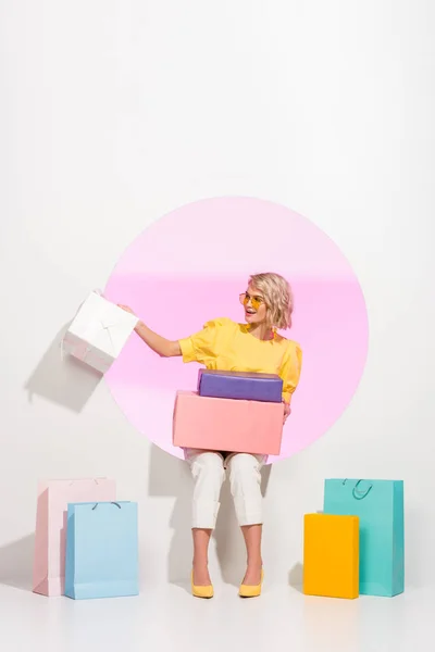 Belle fille à la mode posant avec des boîtes de cadeau colorées et des sacs à provisions sur le blanc avec le cercle rose — Photo de stock