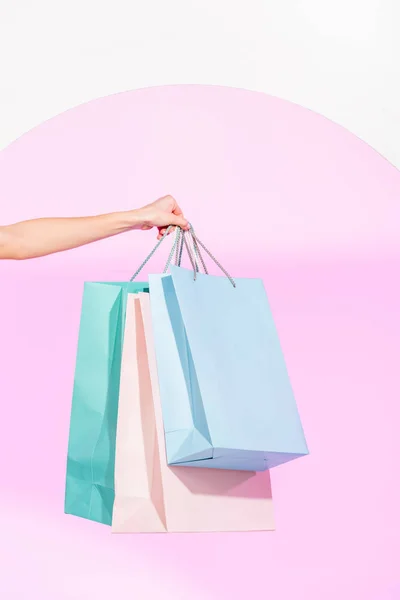 Vista recortada de la mujer joven sosteniendo bolsas de compras de colores en blanco con círculo rosa - foto de stock