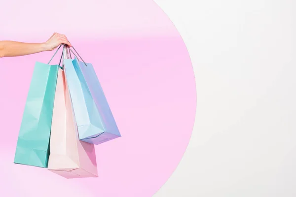 Cropped view of young woman holding colorful shopping bags on white with pink circle — Stock Photo