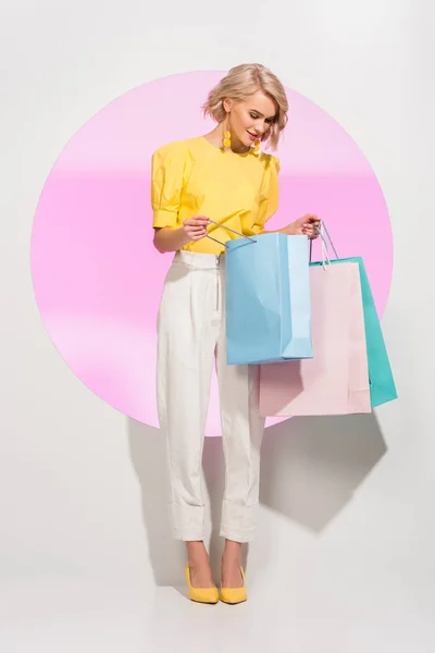 Hermosa chica elegante sosteniendo coloridas bolsas de compras en blanco con círculo rosa - foto de stock