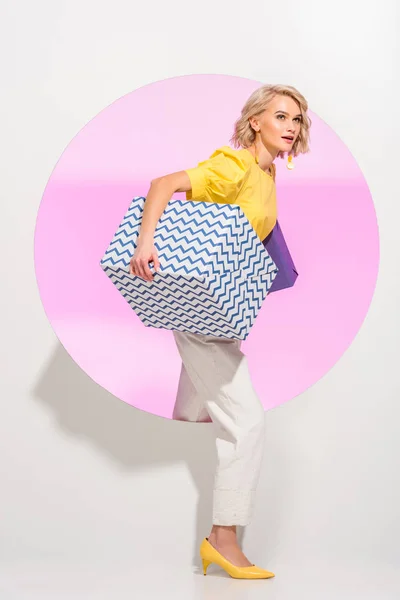 Beautiful stylish young woman holding gift boxes and posing on white with pink circle — Stock Photo