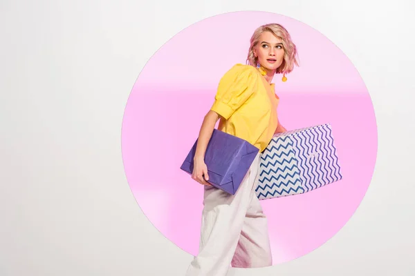 Schöne stilvolle junge Frau hält Geschenkboxen und posiert auf weiß mit rosa Kreis und Kopierraum — Stockfoto