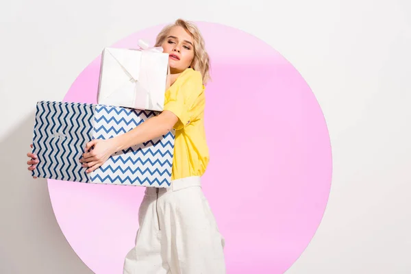 Bella ragazza alla moda che tiene scatole regalo su bianco con cerchio rosa e spazio copia — Stock Photo