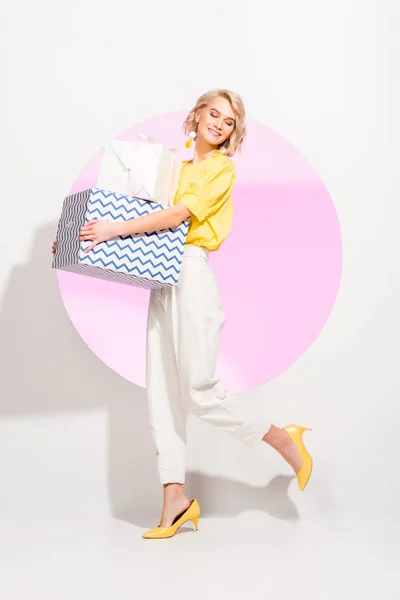 Beautiful fashionable girl holding gift boxes and smiling on white with pink circle — Stock Photo