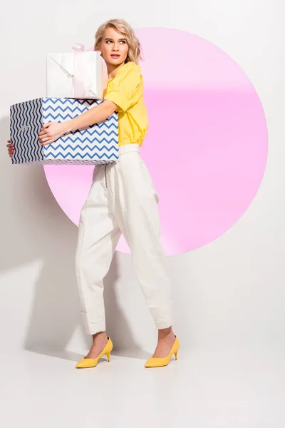 Bella ragazza alla moda che tiene scatole regalo e posa su bianco con cerchio rosa — Stock Photo