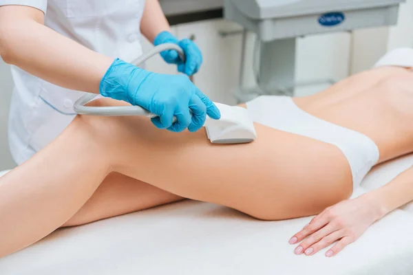 Vista recortada del cosmetólogo con rodillo haciendo masaje de inanición pierna — Stock Photo