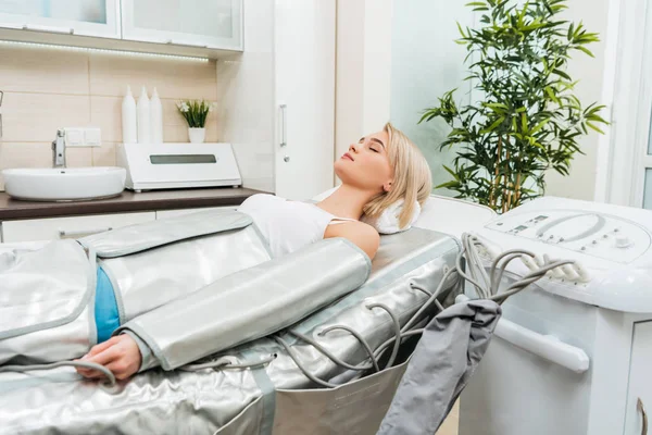 Blonde girl lying with closed eyes during pressotherapy session in clinic — Stock Photo