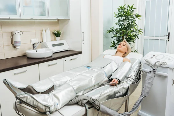 Blonde girl lying on beauty couch during pressotherapy session in clinic — Stock Photo