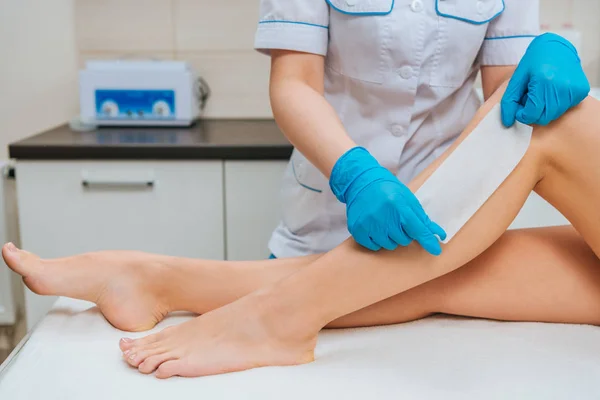 Vista parcial del cosmetólogo con guantes de goma haciendo depilación con cera de pierna - foto de stock