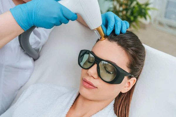 Mujer relajada con gafas protectoras que recibe tratamiento con láser en la clínica - foto de stock