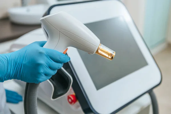 Vista recortada del cosmetólogo en guantes de goma que sostienen el dispositivo láser - foto de stock