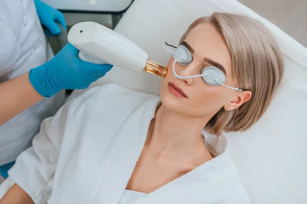 Blonde fille en lunettes de protection recevant un traitement au laser à la clinique — Photo de stock