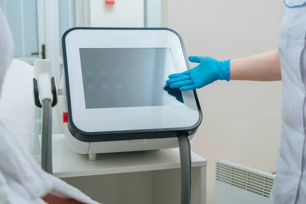 Vista parziale del cosmetologo in gomma guanto toccare macchina laser in clinica — Foto stock