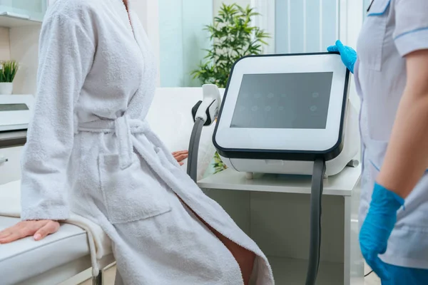 Vue partielle du cosmétologue en gants de caoutchouc touchant la machine laser en clinique — Photo de stock