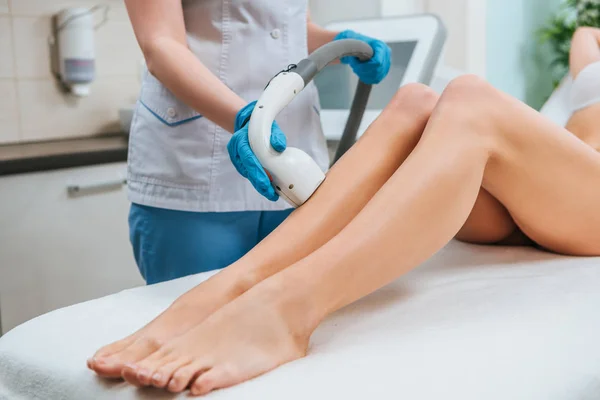 Vista parziale del cosmetologo in guanti di gomma che fa la procedura di depilazione laser sulle gambe — Foto stock