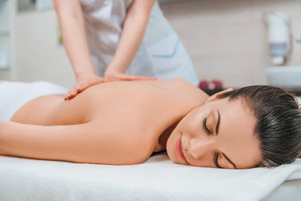 Vista parcial do massagista fazendo massagem nas costas para a menina na mesa de massagem — Fotografia de Stock