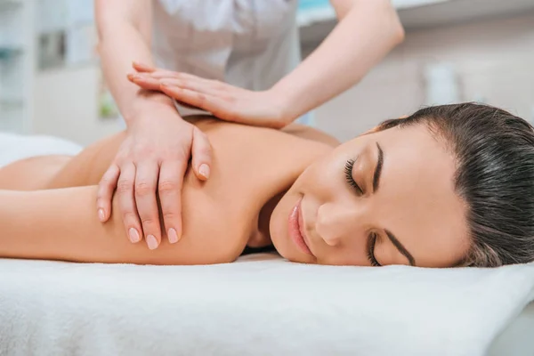 Vista parcial do massagista fazendo massagem nas costas para a menina na mesa de massagem — Fotografia de Stock
