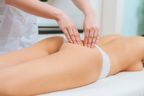 Vista parcial do massagista fazendo massagem nádegas para menina na mesa de massagem — Fotografia de Stock