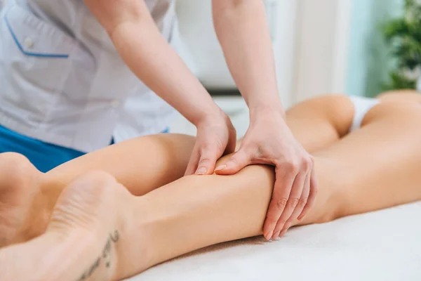 Vista cortada do massagista fazendo massagem nas pernas para a mulher na mesa de massagem — Fotografia de Stock