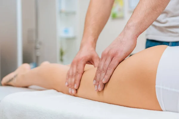 Vista recortada de masajista haciendo masaje de piernas a mujer en mesa de masaje - foto de stock
