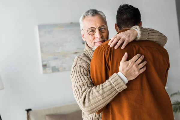 Heureux senior homme en lunettes souriant tout en étreignant fils — Photo de stock