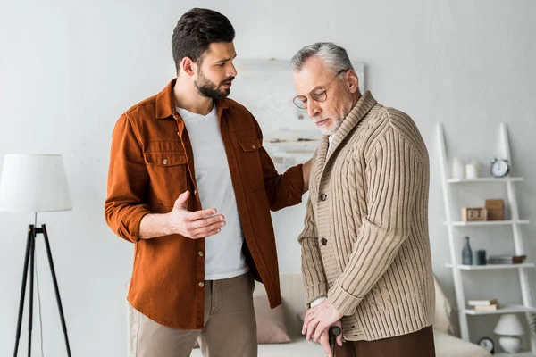 Beau barbu homme geste tout en regardant triste père aîné — Photo de stock