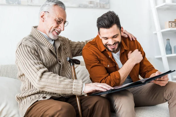 Bel homme souriant tout en tenant album photo près de père aîné — Photo de stock