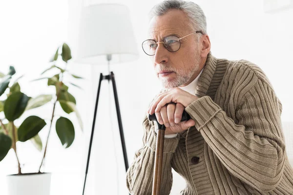 Thoughtful retired man in glasses holding walking stick — Stock Photo