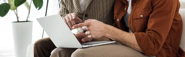 Tiro panorâmico de homem apontando com o dedo para laptop enquanto sentado com o pai sênior — Fotografia de Stock