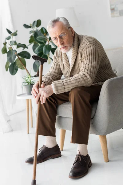 Грустный мужчина в очках сидит в кресле дома — стоковое фото
