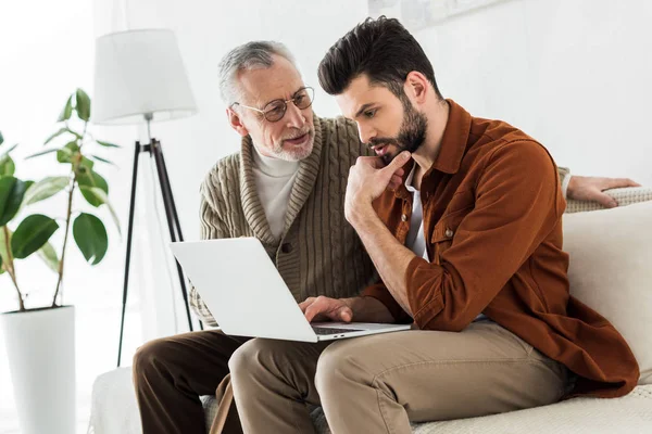 Padre anziano guardando bel figlio seduto con il computer portatile — Foto stock