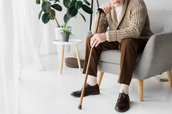Cropped view of retired man sitting in armchair with walking cane — Stock Photo