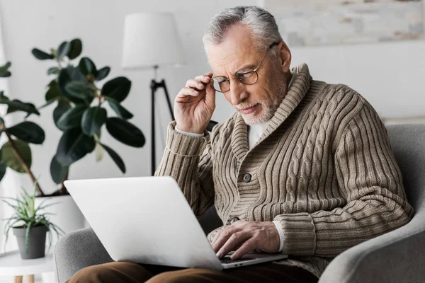 Старший чоловік в окулярах дивиться на ноутбук вдома — стокове фото