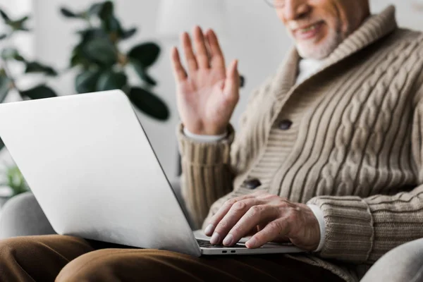 Cropped view of cheerful senior man in glasses waving hand while having video call — Stock Photo